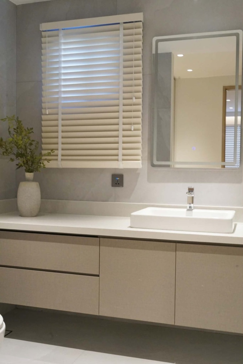 Bathroom vanity with greige drawers, a white basin and a backlit mirror