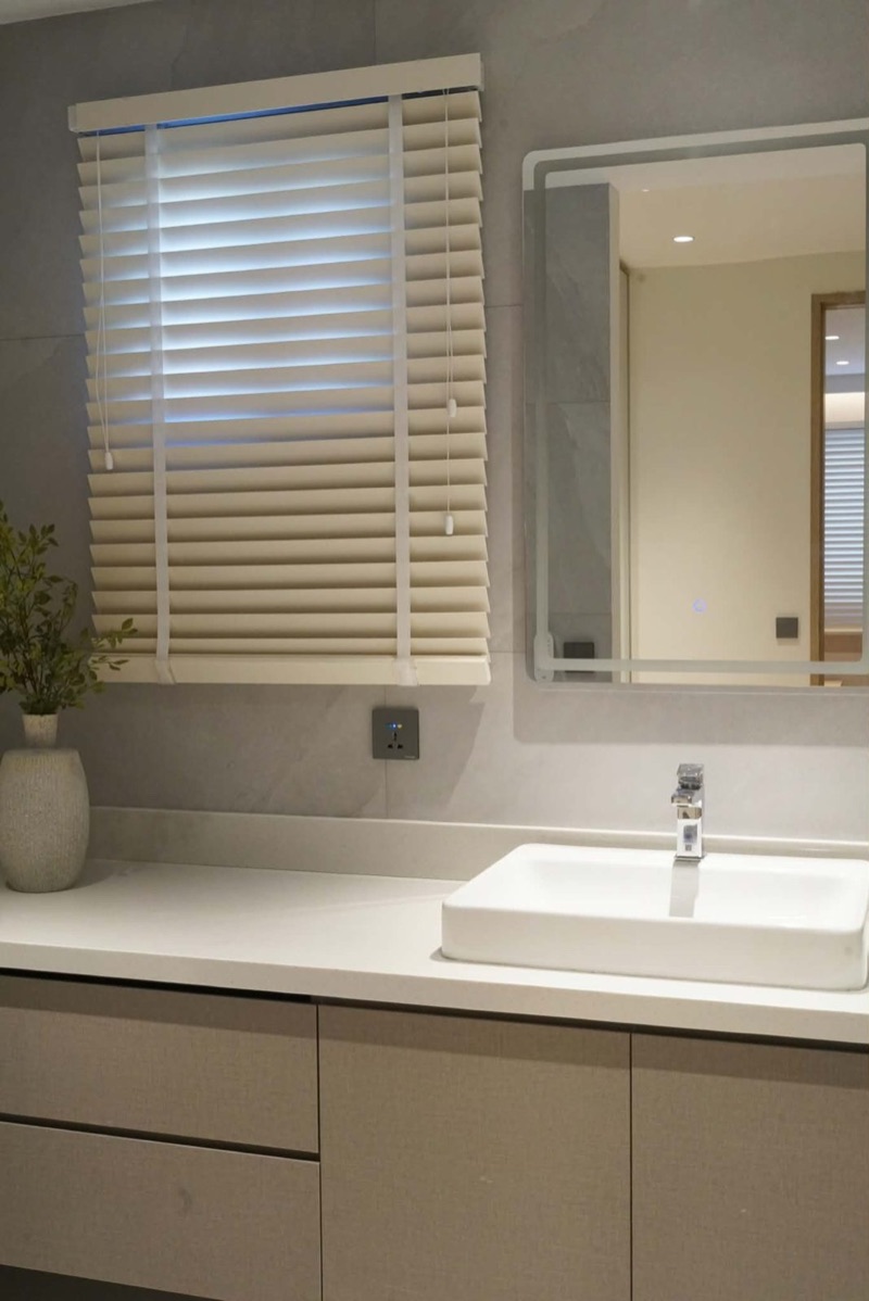 Bathroom vanity with greige drawers under a window with white blinds