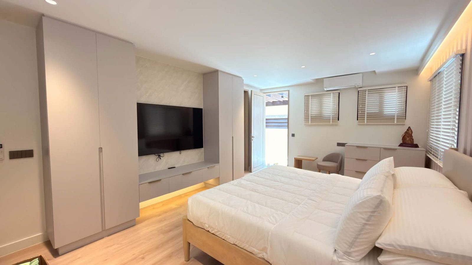 Bedroom with full-height greige wardrobes around a TV niche and warm cove lighting